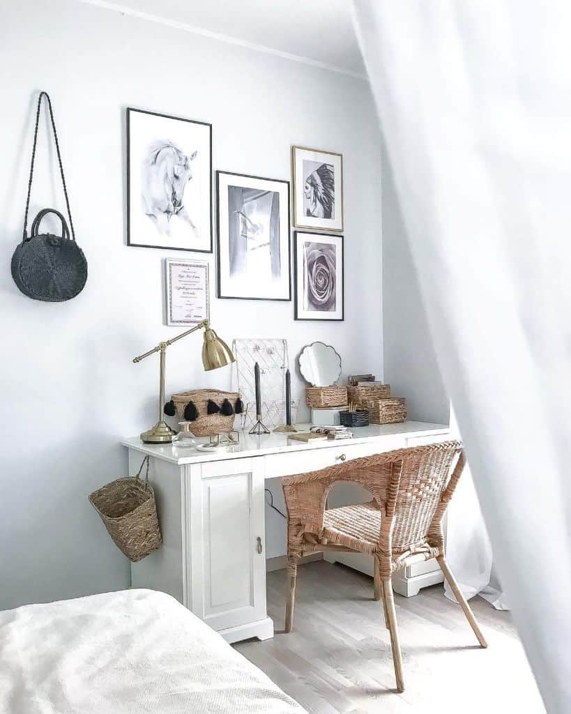 Cozy bedroom workspace with white desk, wicker chair, and framed wall art on white wall.