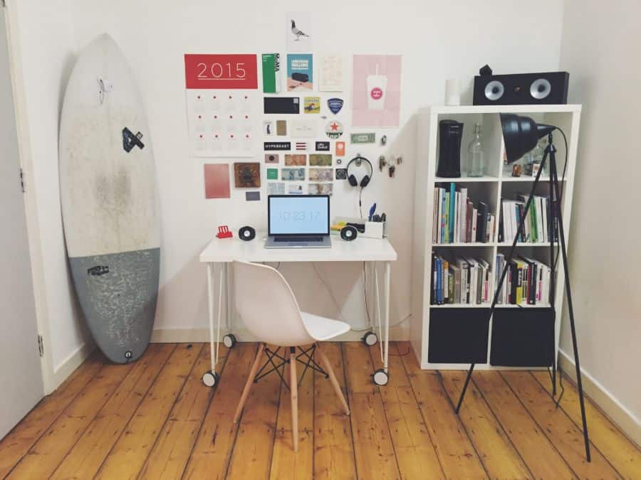 Minimalist home office with surfboard, desk, bookshelf, and decor on wood floor.