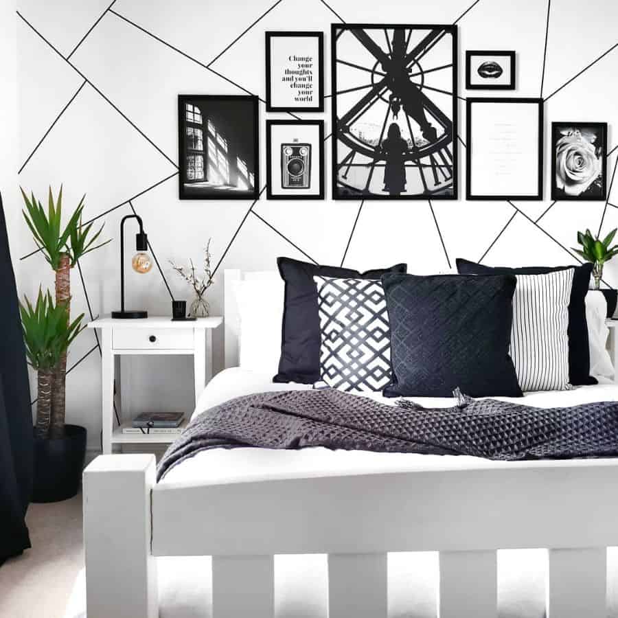 Modern black and white bedroom with geometric wall art, patterned pillows, and a white nightstand.