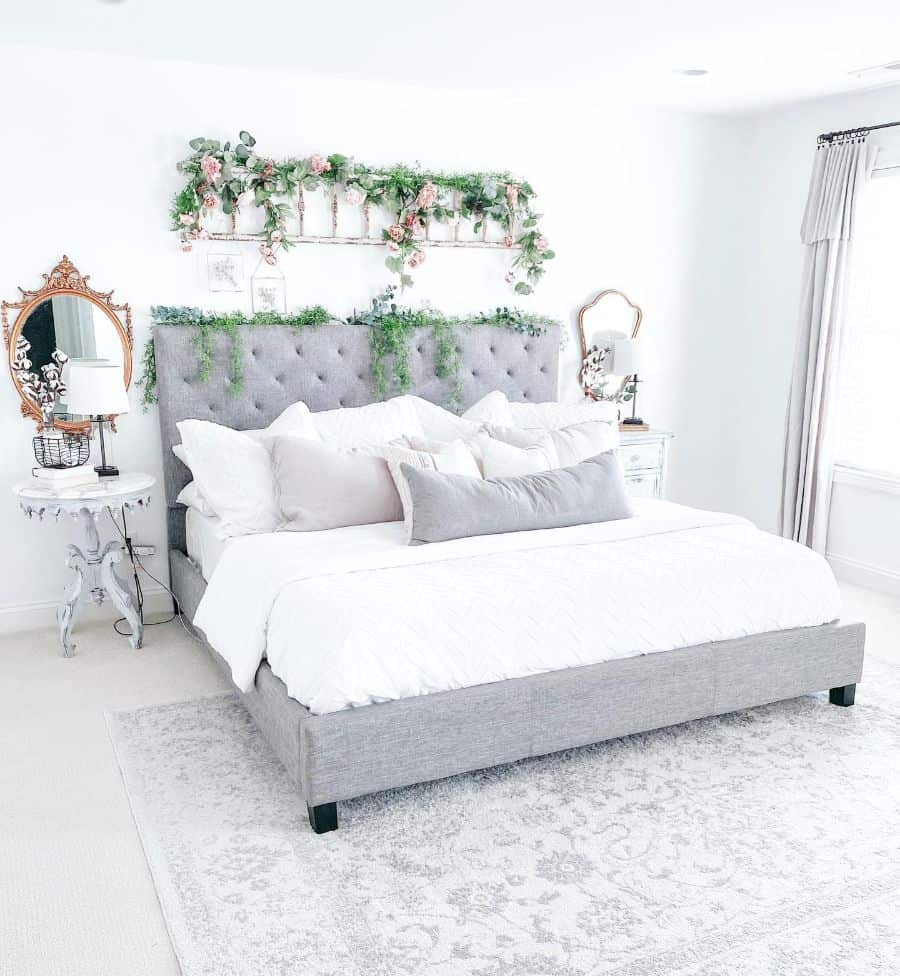 Elegant farmhouse bedroom with a tufted gray bed, white bedding, floral headboard decor, and vintage mirrors