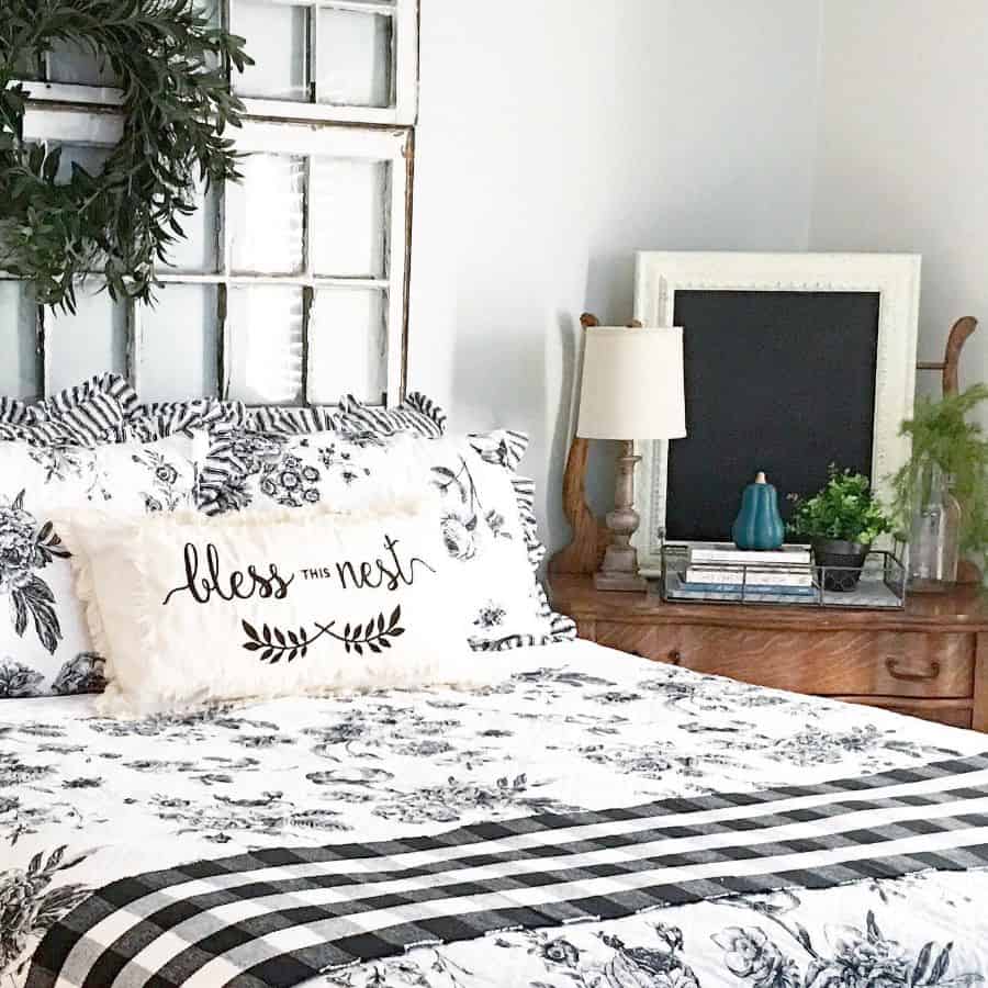 Cozy farmhouse bedroom with floral bedding, "Bless This Nest" pillow, vintage window decor, and a wooden nightstand