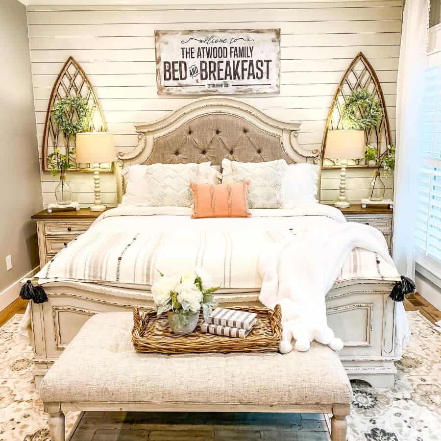 Cozy farmhouse bedroom with a large bed, decorative pillows, and a rustic sign above: light-filled and warmly decorated