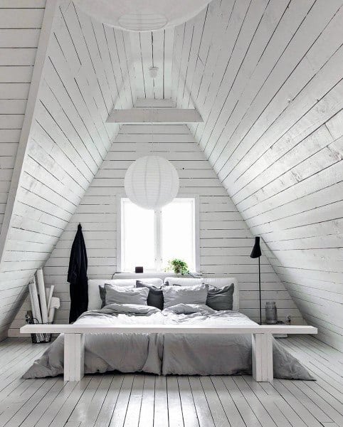 Minimalist A-frame attic bedroom with white wooden walls, a bed with gray bedding, and a round paper lantern above