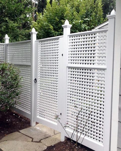 White trellis privacy fence with decorative caps surrounded by greenery in a backyard.