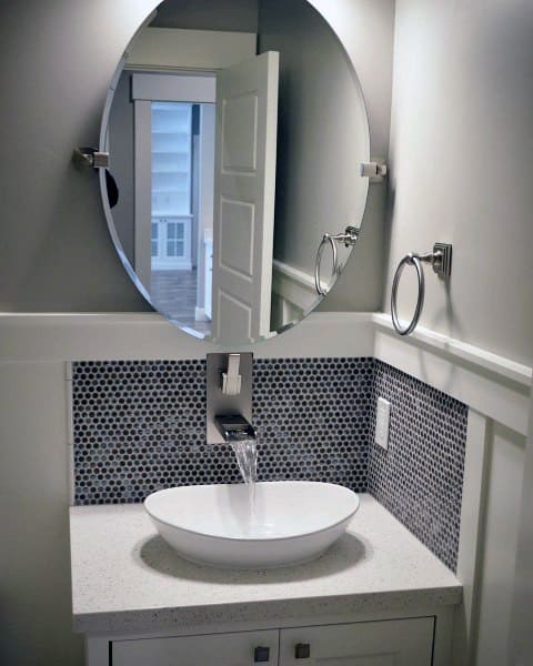 Modern half bath with round mirror, white basin, and flowing faucet, hexagonal tile backsplash under soft lighting