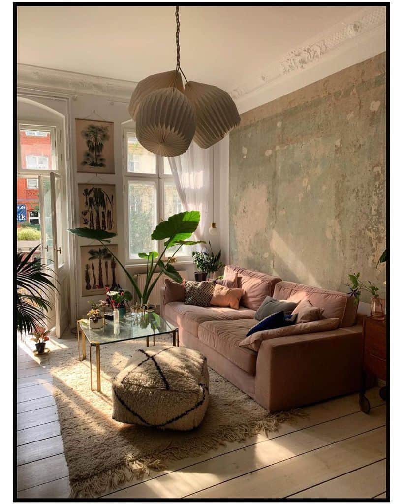 Cozy living room with a pink sofa, large plants, a glass coffee table, and sunlight streaming through windows