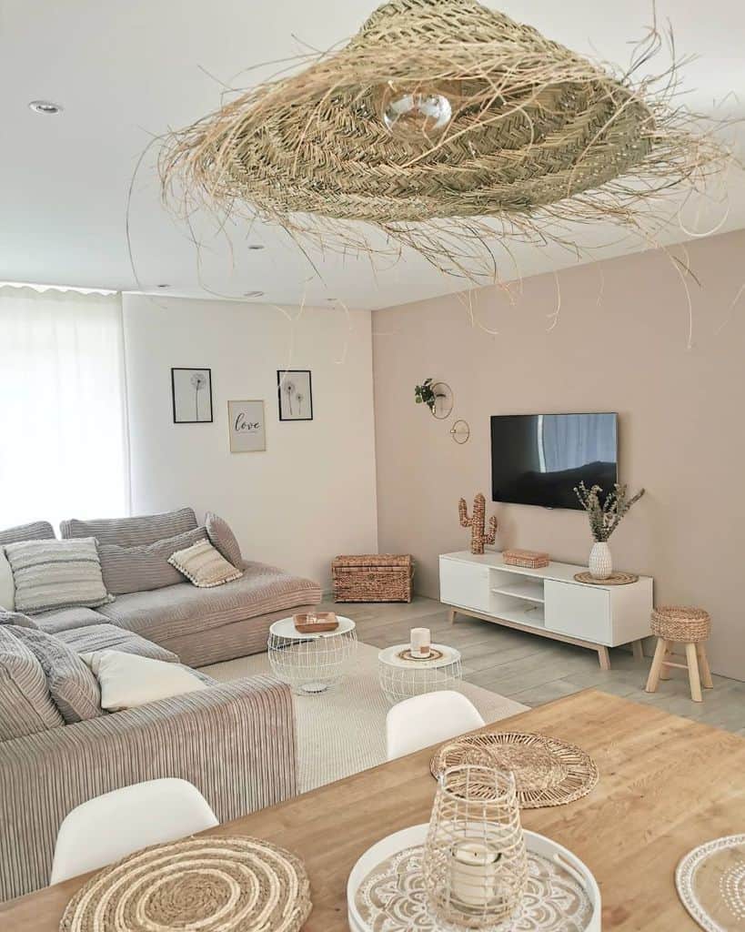 Cozy living room with a beige sofa, TV, wicker accents, and a rustic dining table under a woven light fixture