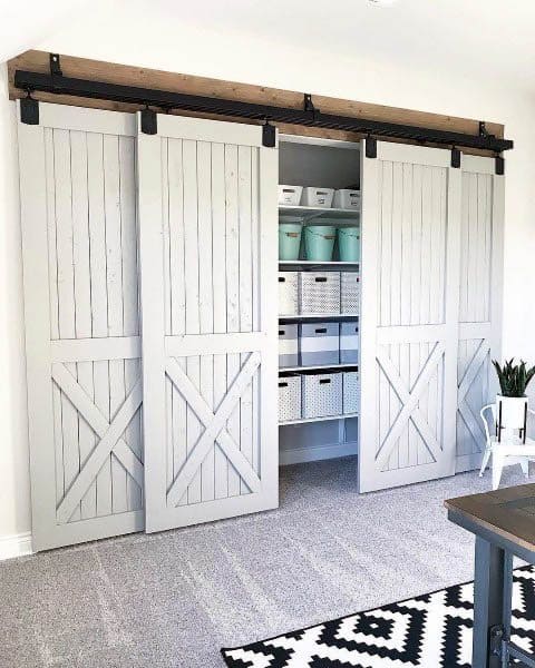 A stylish sliding barn door closet with white wooden panels and organized storage bins inside