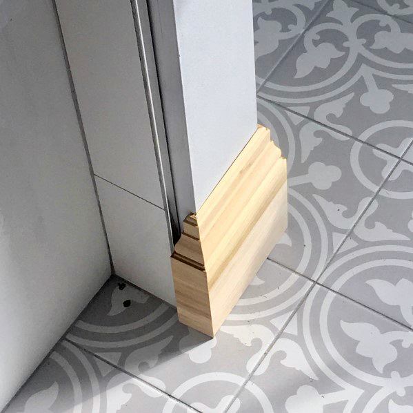 Decorative light wood baseboard with patterned gray and white tile flooring.