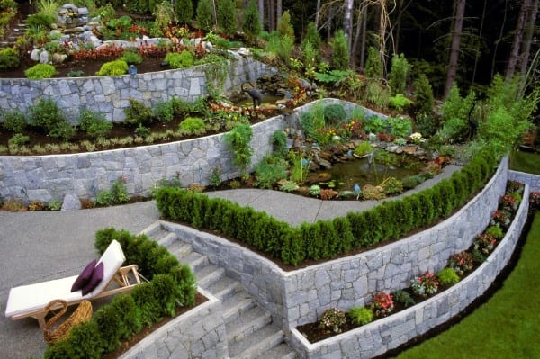 Multi-tiered stone retaining walls with landscaped gardens, a pond, and integrated stairs.