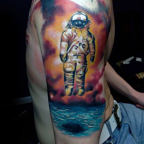 Deja Entendu astronaut tattoo with vivid stormy sky and glowing ocean, creating a dramatic and surreal floating effect.