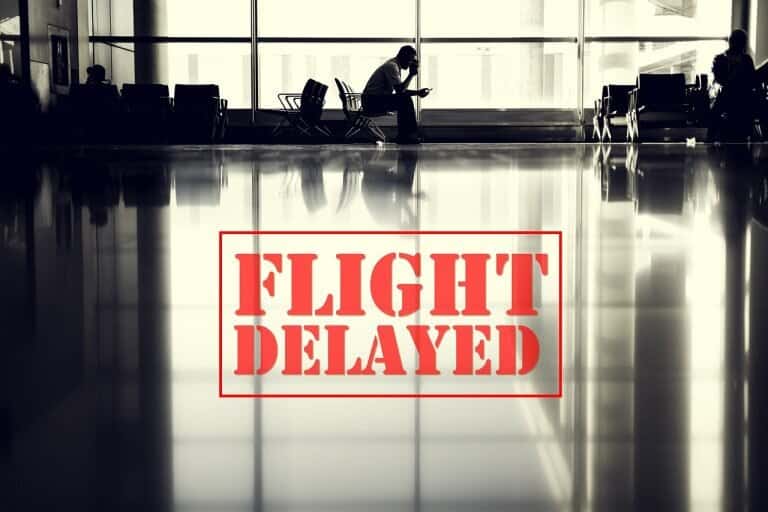 A person sits alone in an empty airport terminal with FLIGHT DELAYED in bold red letters over the image