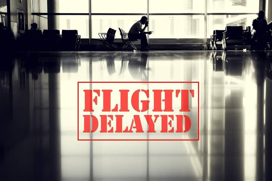 A person sits alone in an empty airport terminal with FLIGHT DELAYED in bold red letters over the image