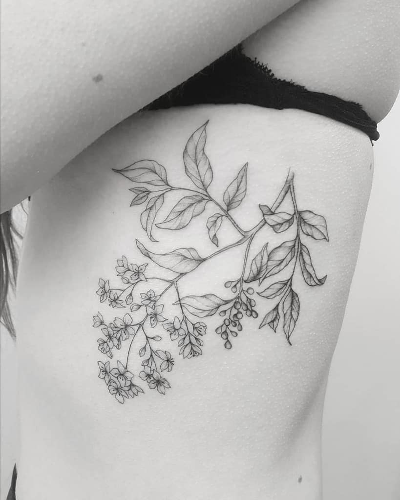 Delicate fine-line botanical tattoo of a blooming branch with leaves, flowers, and berries