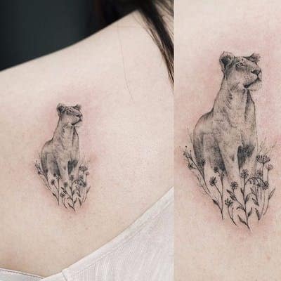 Small, delicate lioness tattoo on the upper back, featuring fine shading and floral details for a minimalist yet elegant design.