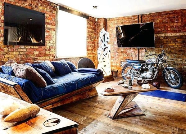 Denim couch with wooden frame in an industrial-style living room with exposed brick walls and a motorcycle display.