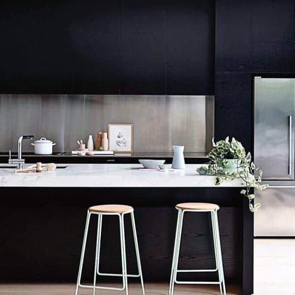 Modern black kitchen cabinets with stainless steel backsplash, white countertop, and bar stools.
