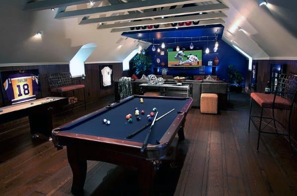 Attic game room with pool table, sports decor, large TV, and cozy seating area.