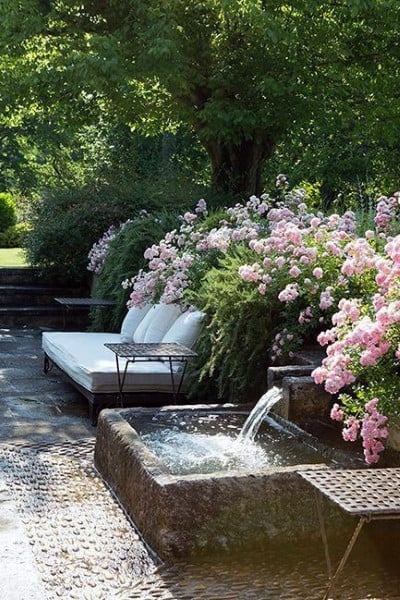 Charming backyard with a concrete waterfall pond, blooming pink roses, and cozy seating area.