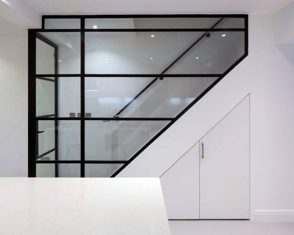 Modern staircase with glass wall and minimalist under-the-stairs storage cabinet in a white interior.