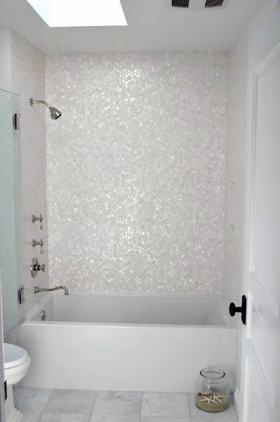 White bathtub with pearl-like mosaic tile accent wall and natural light from skylight.