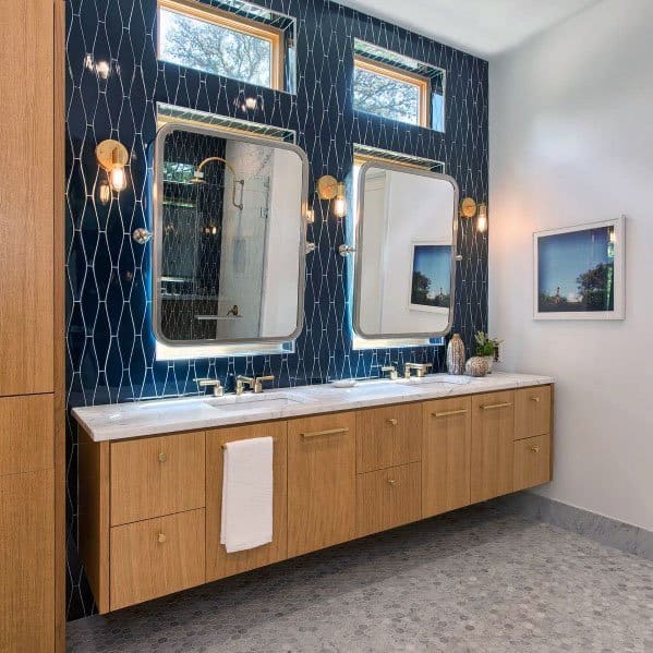 Bathroom with navy blue patterned tile wall, floating wood vanity, and gold fixtures.