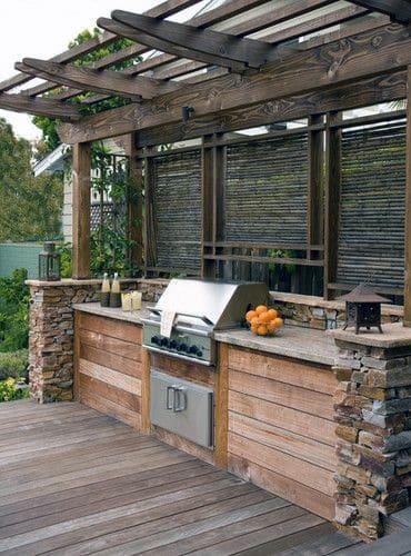 Outdoor kitchen with a wooden pergola, built-in stainless steel grill, and a rustic stone counter with oranges on top