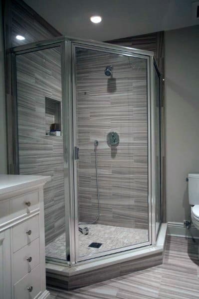 Modern bathroom with a corner glass-enclosed shower, beige wood-patterned tiles, and a white cabinet next to the toilet