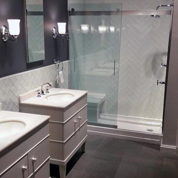 Modern grey bathroom with herringbone tiles, dual sinks, and glass shower.