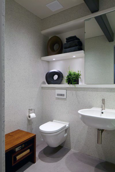 Minimalist half bath with wall-mounted toilet, sink, and shelves for towels, decor, and a plant