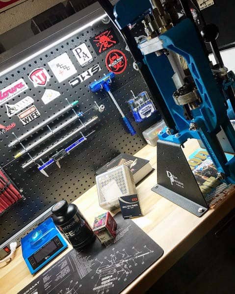 Compact reloading bench with a blue press, pegboard tool organization, and reloading accessories neatly arranged