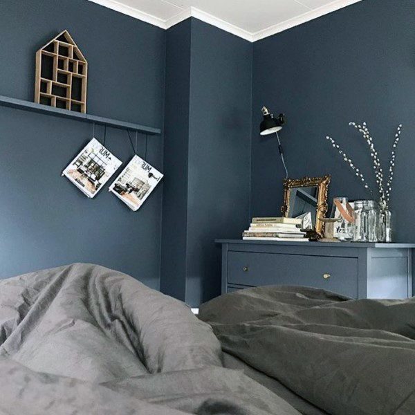 Cozy navy bedroom with gray bedding, floating shelf, and decorative dresser accents.