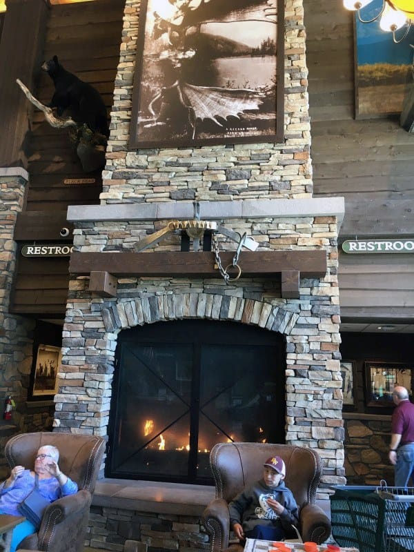 Rustic stone fireplace with wooden mantel, decorative tools, and cozy leather armchairs.