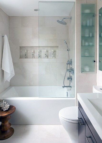 Bathtub with glossy porcelain tiles, glass shower door, and built-in niche for toiletries.