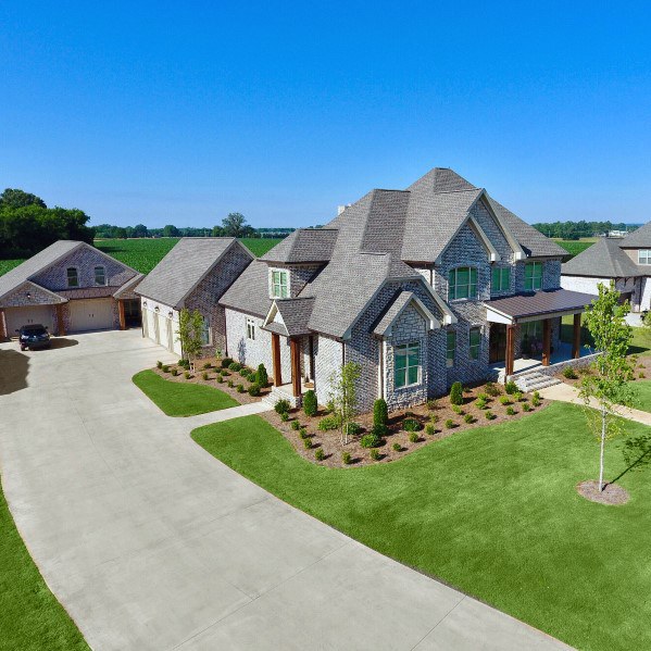 Sprawling estate with brick and stone exterior, gabled rooflines, manicured landscaping, and a detached garage on a spacious property