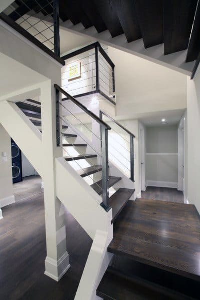 Modern staircase with dark wood steps and black cable railing in a bright open hallway.