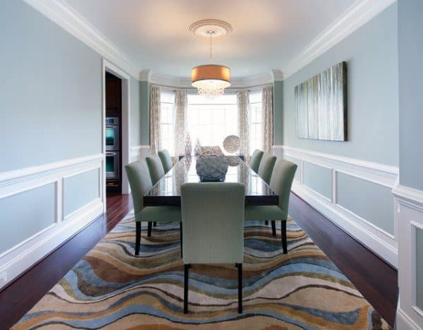 Elegant dining room with blue walls, white chair rail molding, modern art, and a patterned rug for a sophisticated ambiance