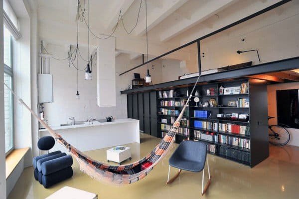 Patterned hammock in a modern loft apartment with bookshelves and an open kitchen layout.