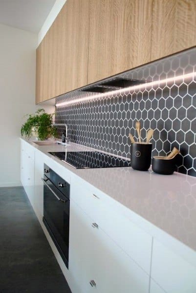 Modern kitchen with white countertops wooden cabinets and black hexagon backsplash tiles.