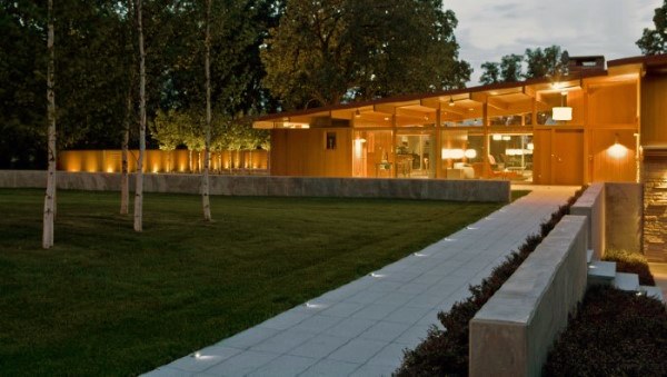 Modern home with glass walls, illuminated pathway, manicured lawn, and minimalist landscaping.