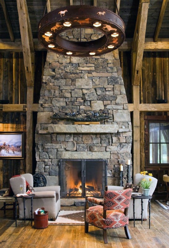 Rustic cabin with large stone fireplace, patterned chairs, and unique circular chandelier.