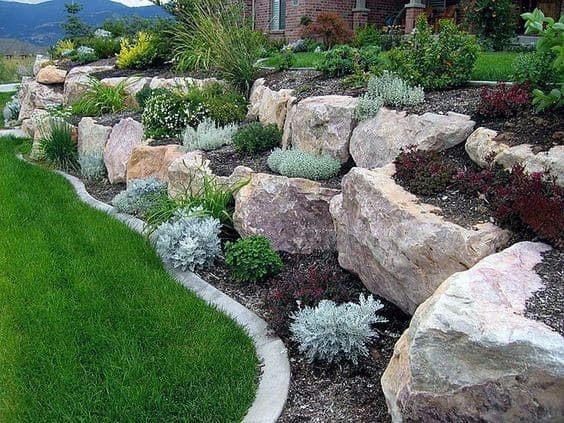 Sloped garden with large boulders, lush plants, and a curved lawn edge, creating a natural and visually appealing hillside design