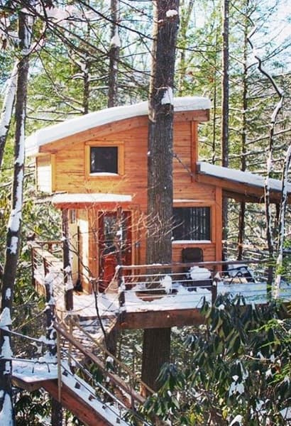Snow-covered wooden treehouse nestled among tall trees in a forest