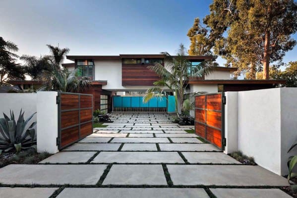 Modern house with wooden accents, palm trees, and open gate leading to a stone pathway