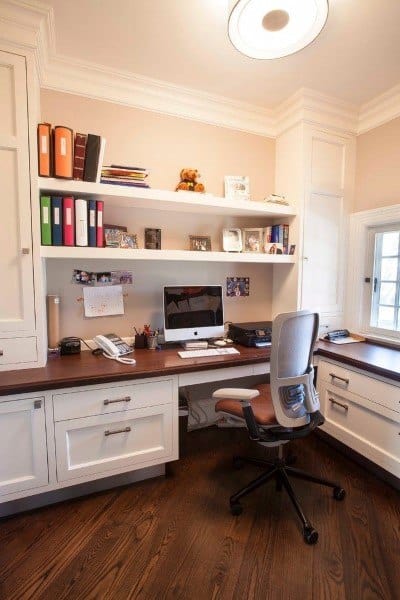 Home office with a computer, swivel chair, shelves with binders, and decor on a wooden built-in desk