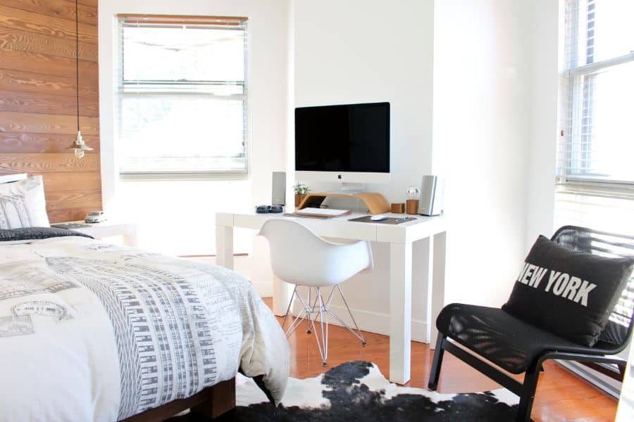Bright bedroom workspace with white desk, computer, and black accent chair.