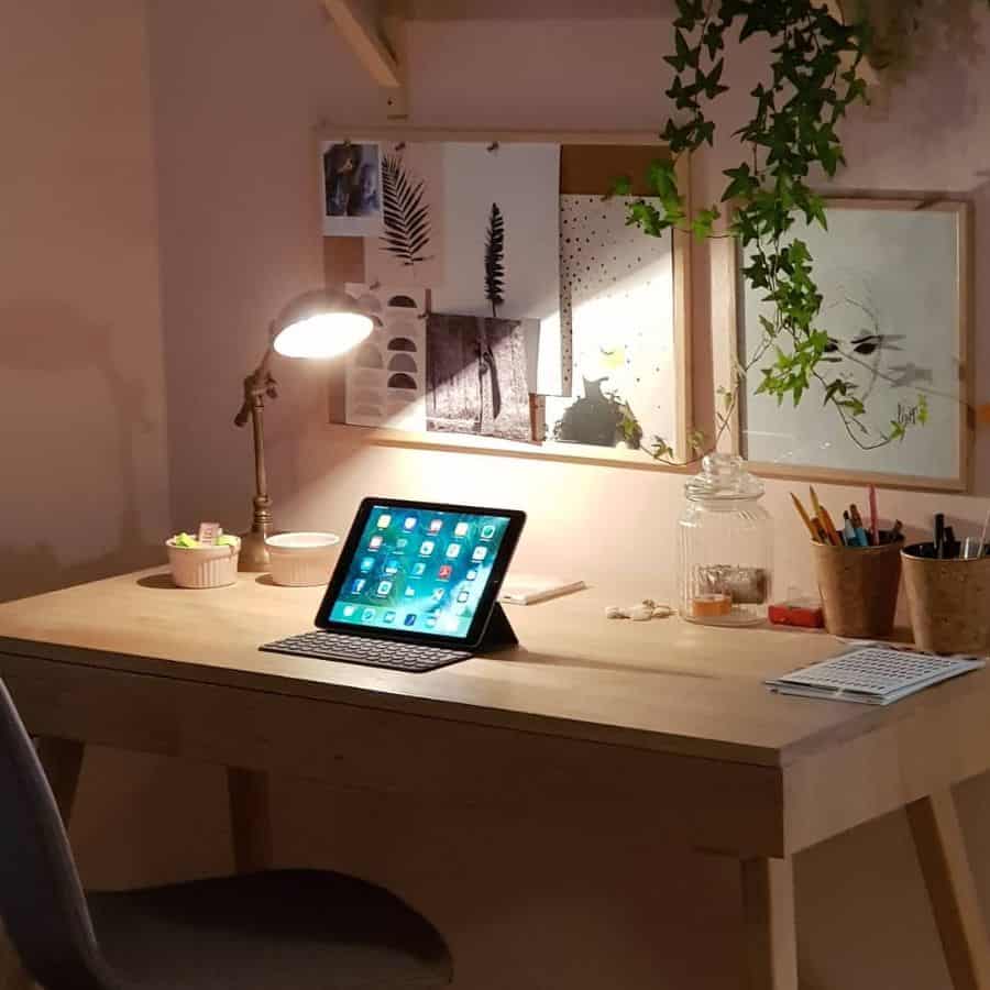 Cozy workspace with wooden desk, tablet, desk lamp, and nature-inspired wall decor.