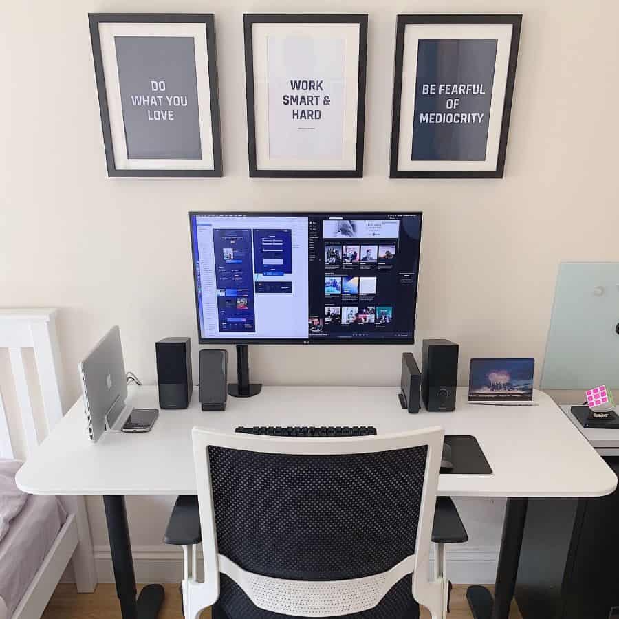 Modern office desk with monitor, laptop, and motivational framed wall art.