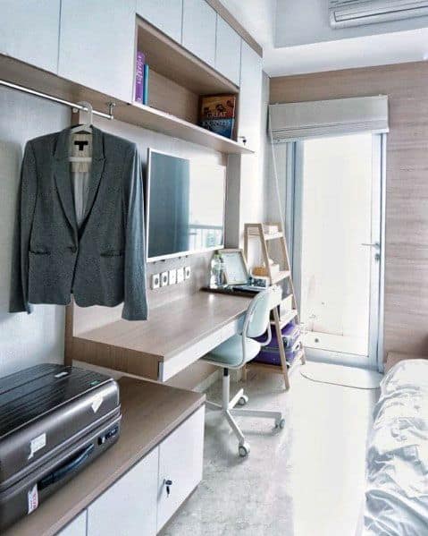 Compact studio with built-in desk, storage cabinets, hanging space, and balcony access.