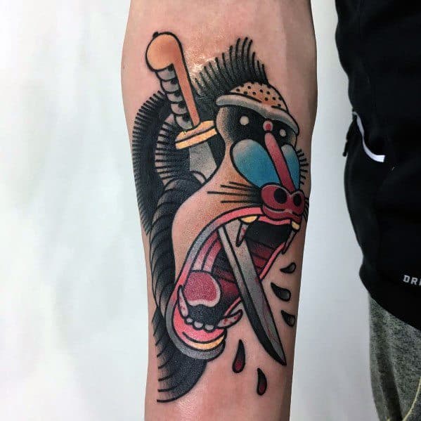 Neo-traditional baboon tattoo with bold colors, fierce expression, and a dagger through its mouth, creating a dramatic and striking forearm design.
